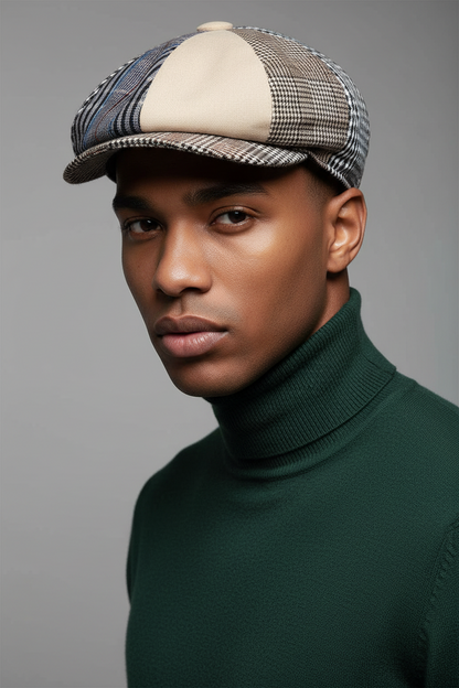 A man wearing a multi-patterned flat cap with beige, brown, and blue tones, paired with a dark green turtleneck sweater, photographed against a solid gray background.