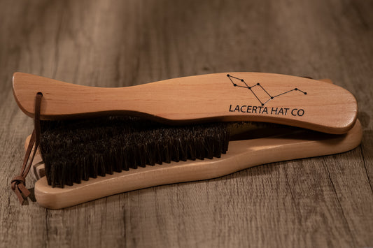 A horsehair brim brush with a wooden handle and black bristles, resting on a wooden surface.