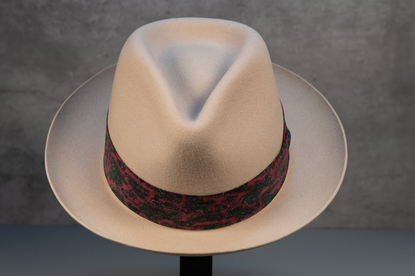 A bone white rabbit fur fedora hat with a decorative band on a stand against a neutral background.