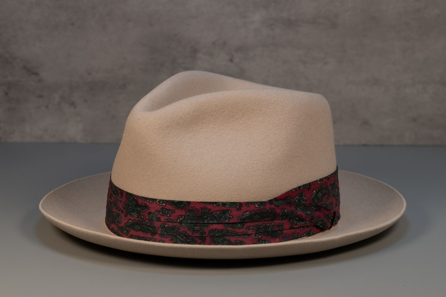 bone white rabbit fur fedora hat with a red and green paisley band on a neutral background.