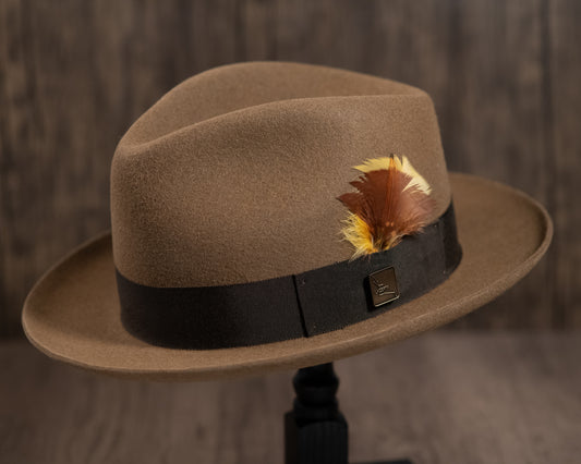 A camel-colored fur felt hat with a khaki green grosgrain ribbon and a feather accent, displayed on a stand.