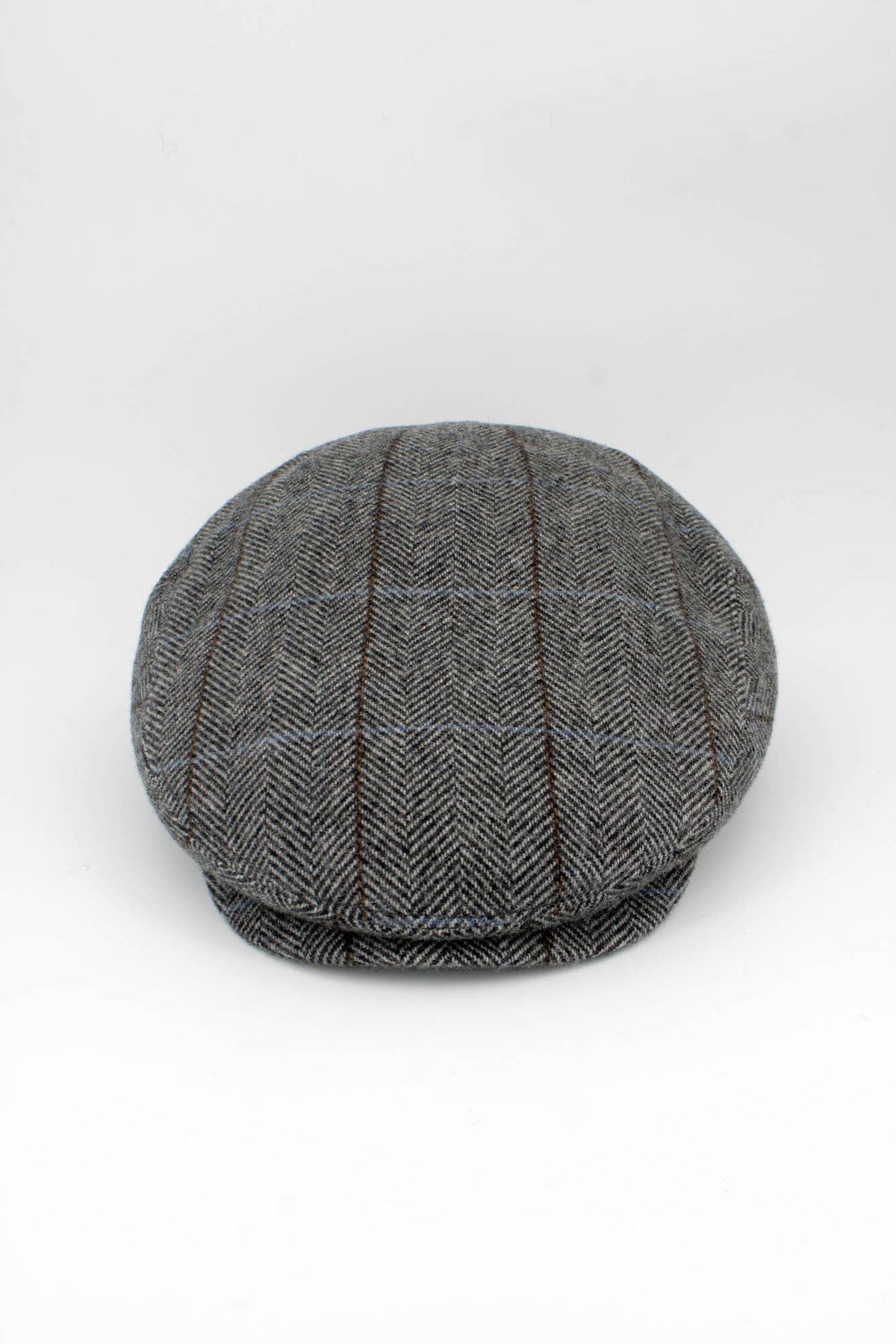 A classic flat cap in a gray and black herringbone pattern with subtle brown and blue windowpane lines, photographed on a seamless white background.