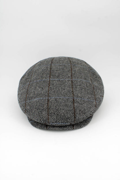 A classic flat cap in a gray and black herringbone pattern with subtle brown and blue windowpane lines, photographed on a seamless white background.
