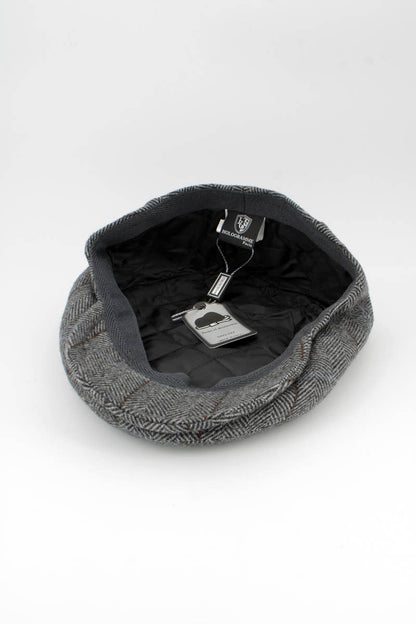 A gray herringbone flat cap shown from an overhead angle, with its black interior lining and attached retail tags visible against a clean white background.