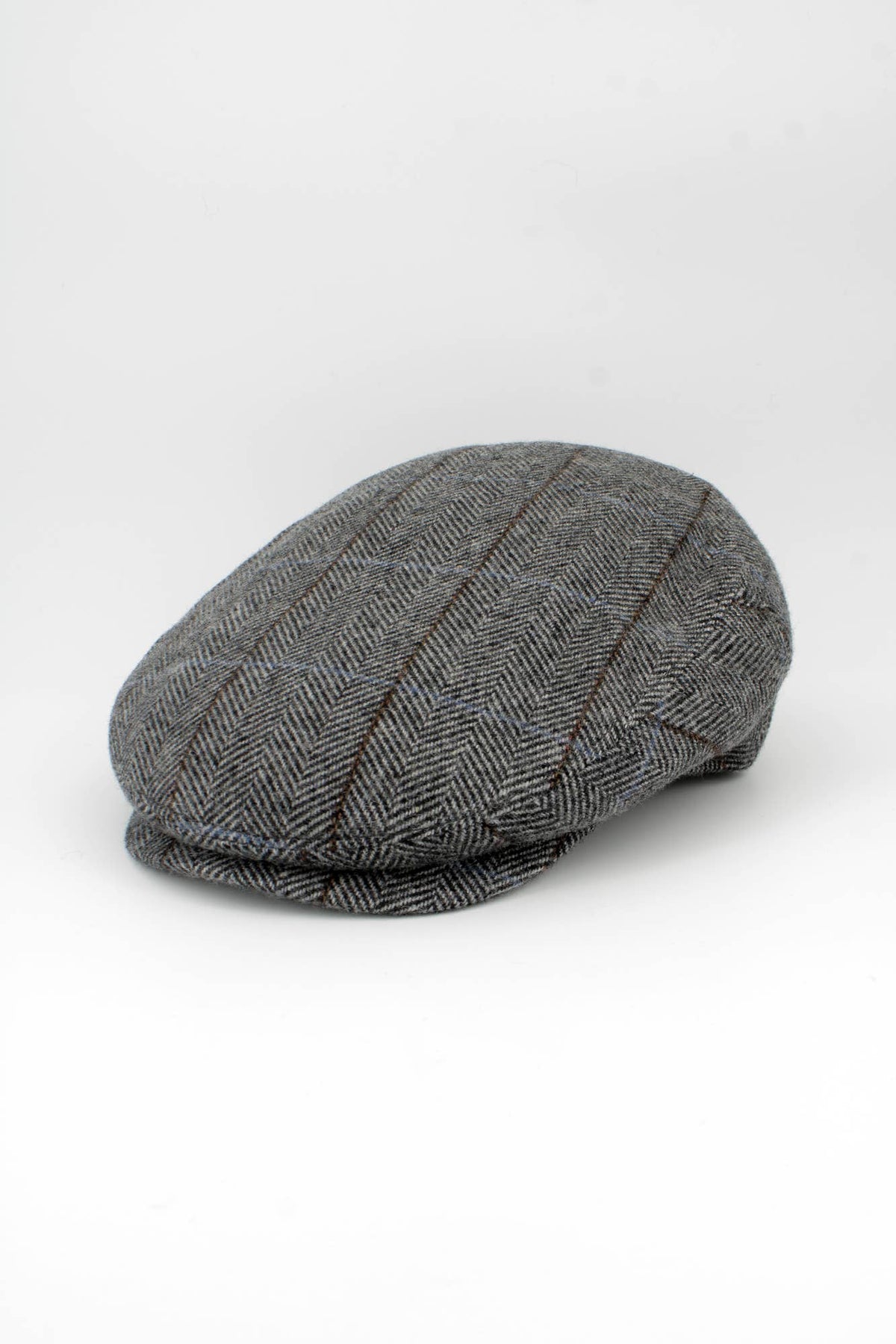 A classic flat cap in a gray and black herringbone pattern with subtle brown stripes, photographed on a seamless white studio background.