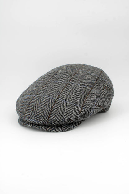 A classic flat cap in a gray and black herringbone pattern with subtle brown stripes, photographed on a seamless white studio background.