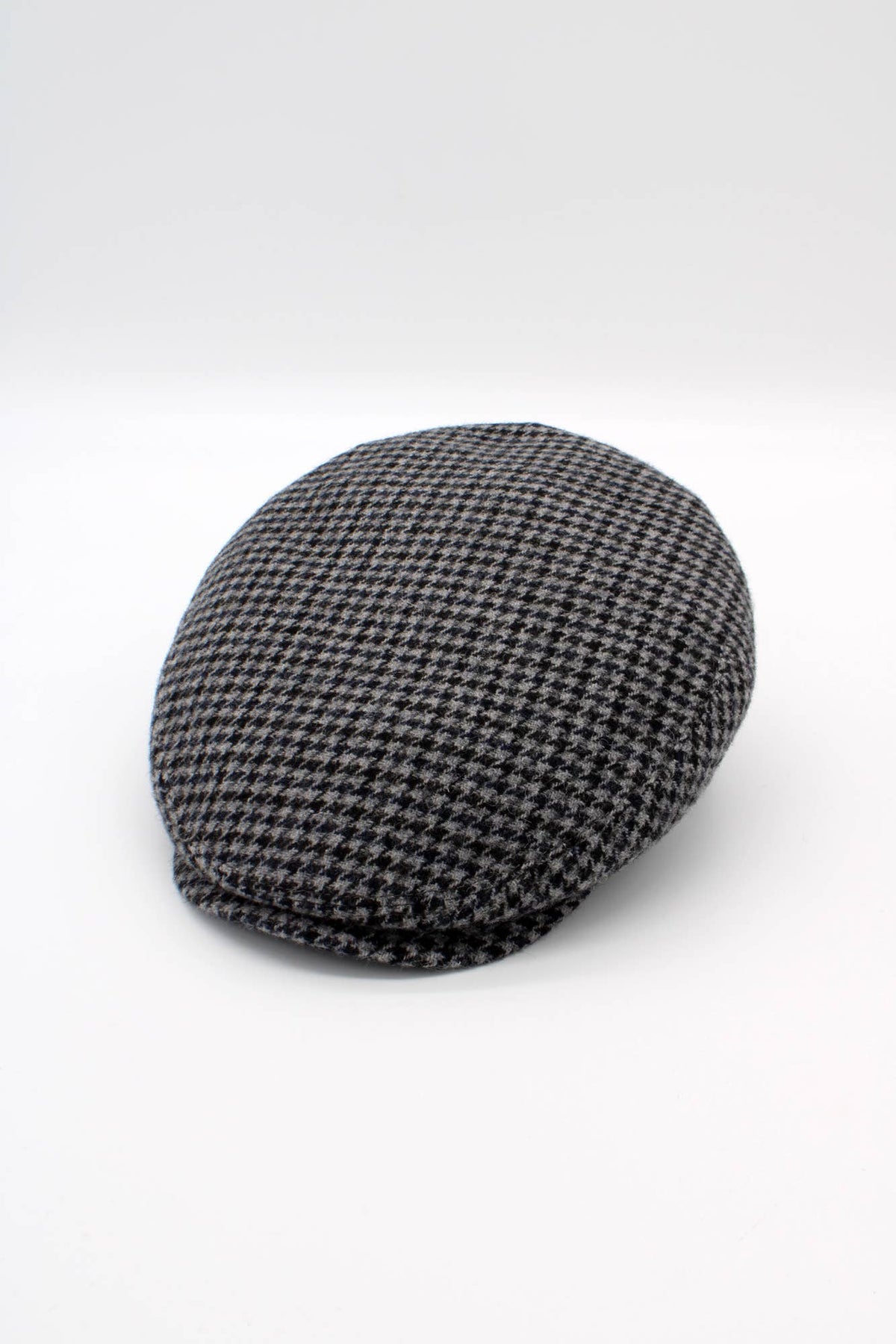 A classic flat cap in a black and gray houndstooth pattern, photographed on a seamless light gray studio background.
