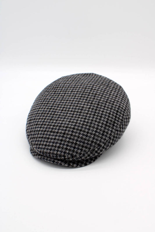 A classic flat cap in a black and gray houndstooth pattern, photographed on a seamless light gray studio background.