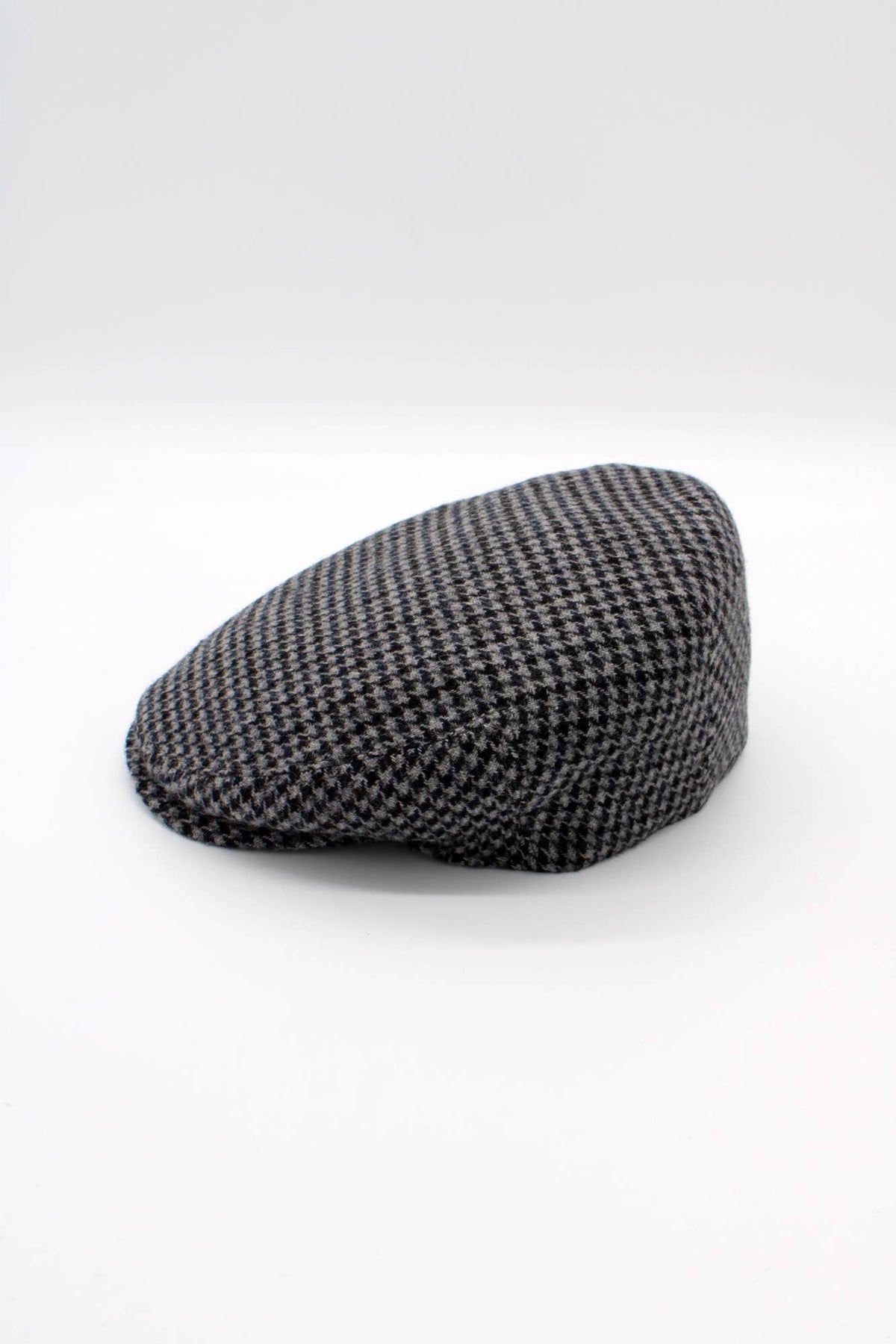 A classic flat cap in a black and white houndstooth pattern, photographed on a seamless light gray studio background.