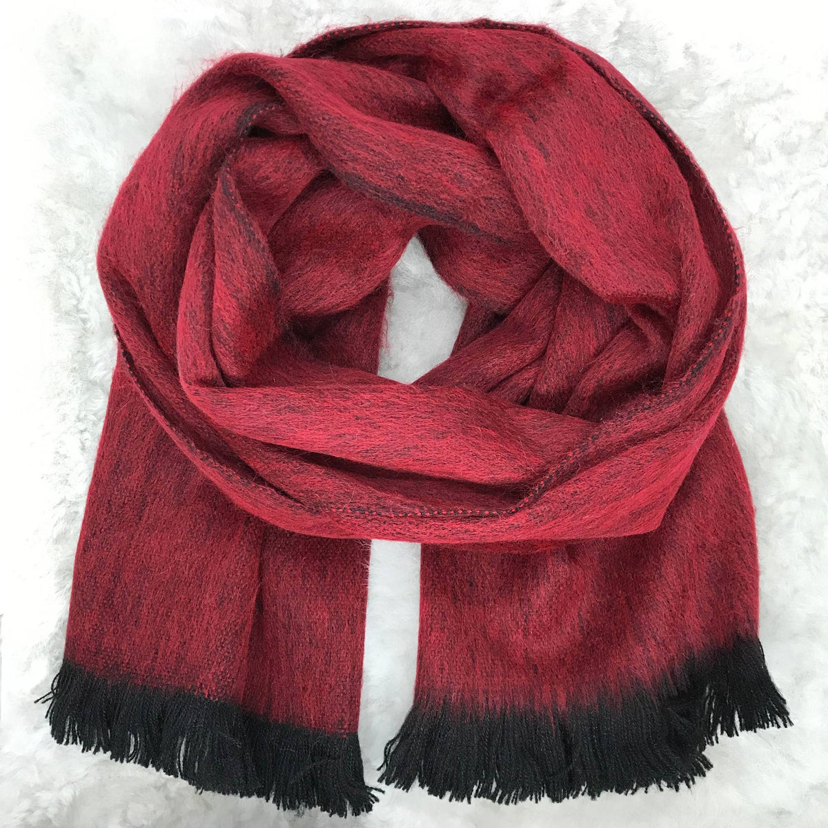 A red and black ombre scarf with fringed ends, styled in a loop on a white textured background.