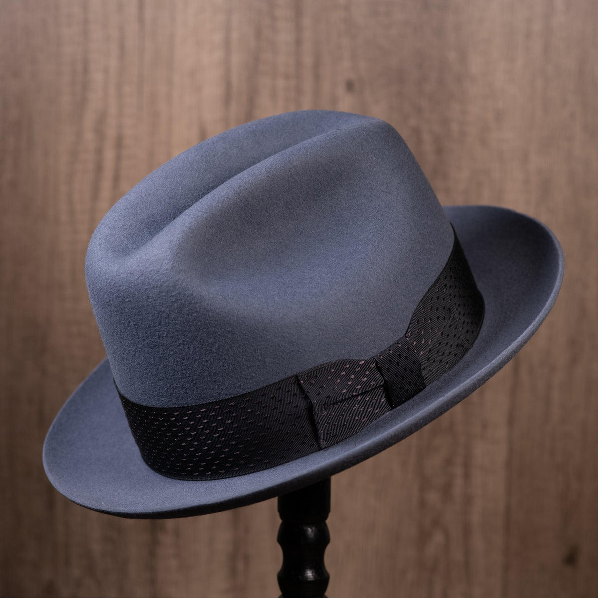 A steel grey rabbit fur felt hat with a vintage navy blue embroidered stripe dot ribbon hatband, displayed on a stand with a wooden background.